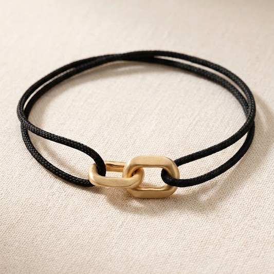 Link Bracelet in 14-karat solid gold on a black woven cord, laid flat on linen