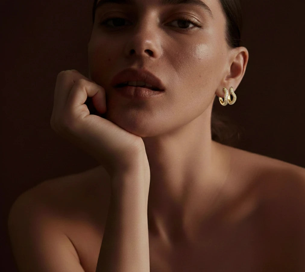 Model wearing gold hoop earrings, chin resting on hand